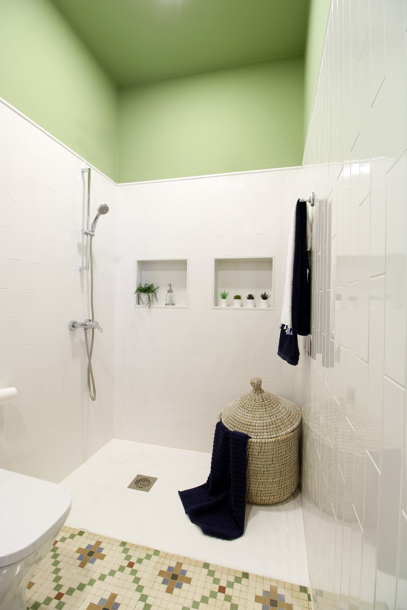Amplia ducha, pared mitad superior verde, suelo con mosaicos