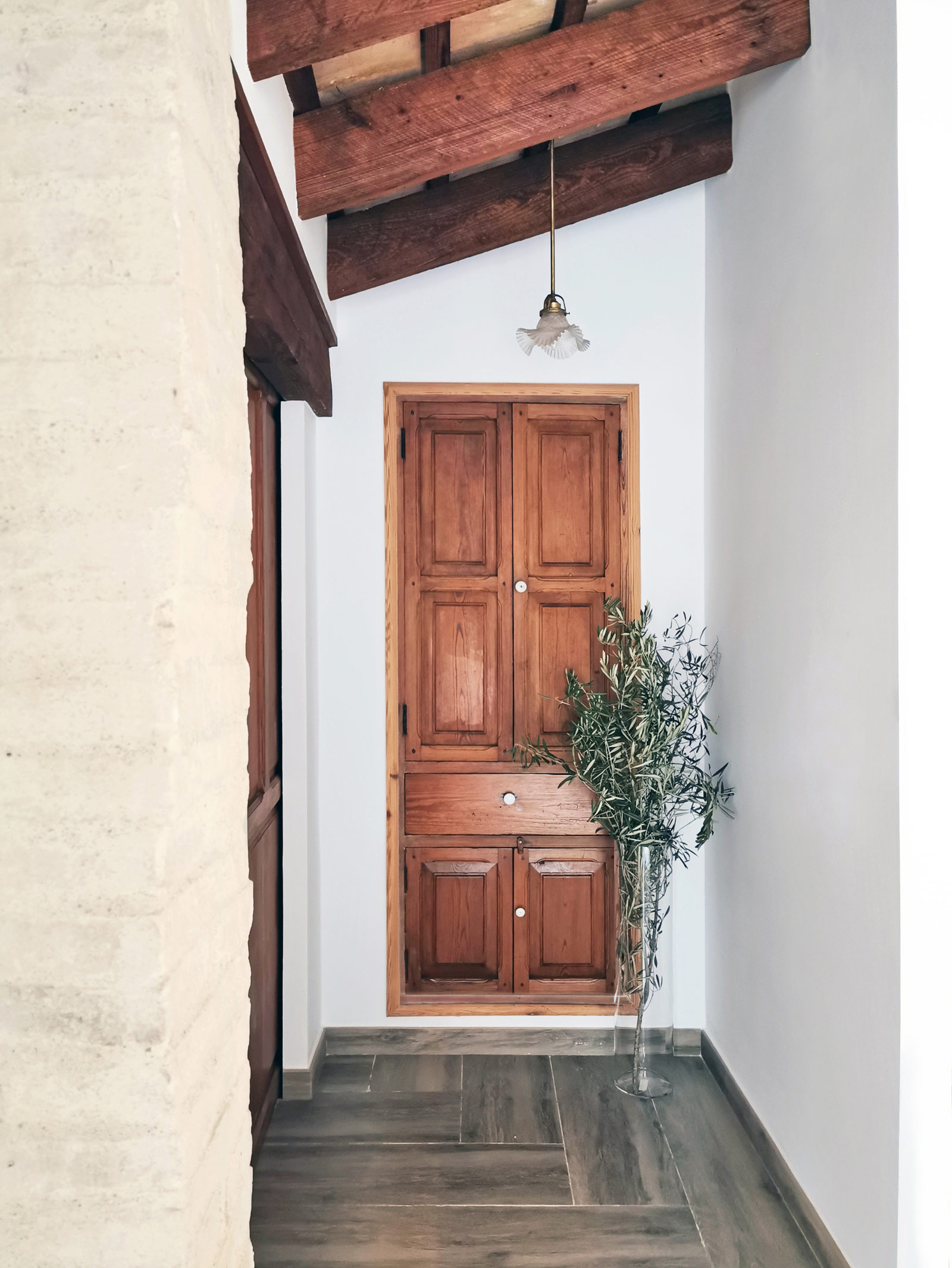 Pasillo con puerta de madera, paredes blancas, techos altos inclinados con vigas de madera