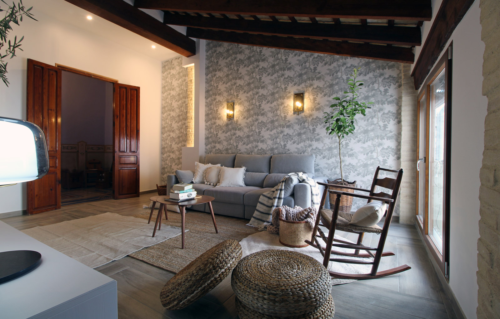 Salón con granes puertas de madera, silla balancín, sofá con cojines y manta