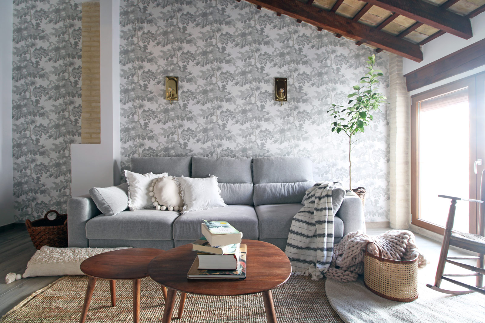 Salón luminoso con papel pintado, sofá gris y techo con vigas inclinado