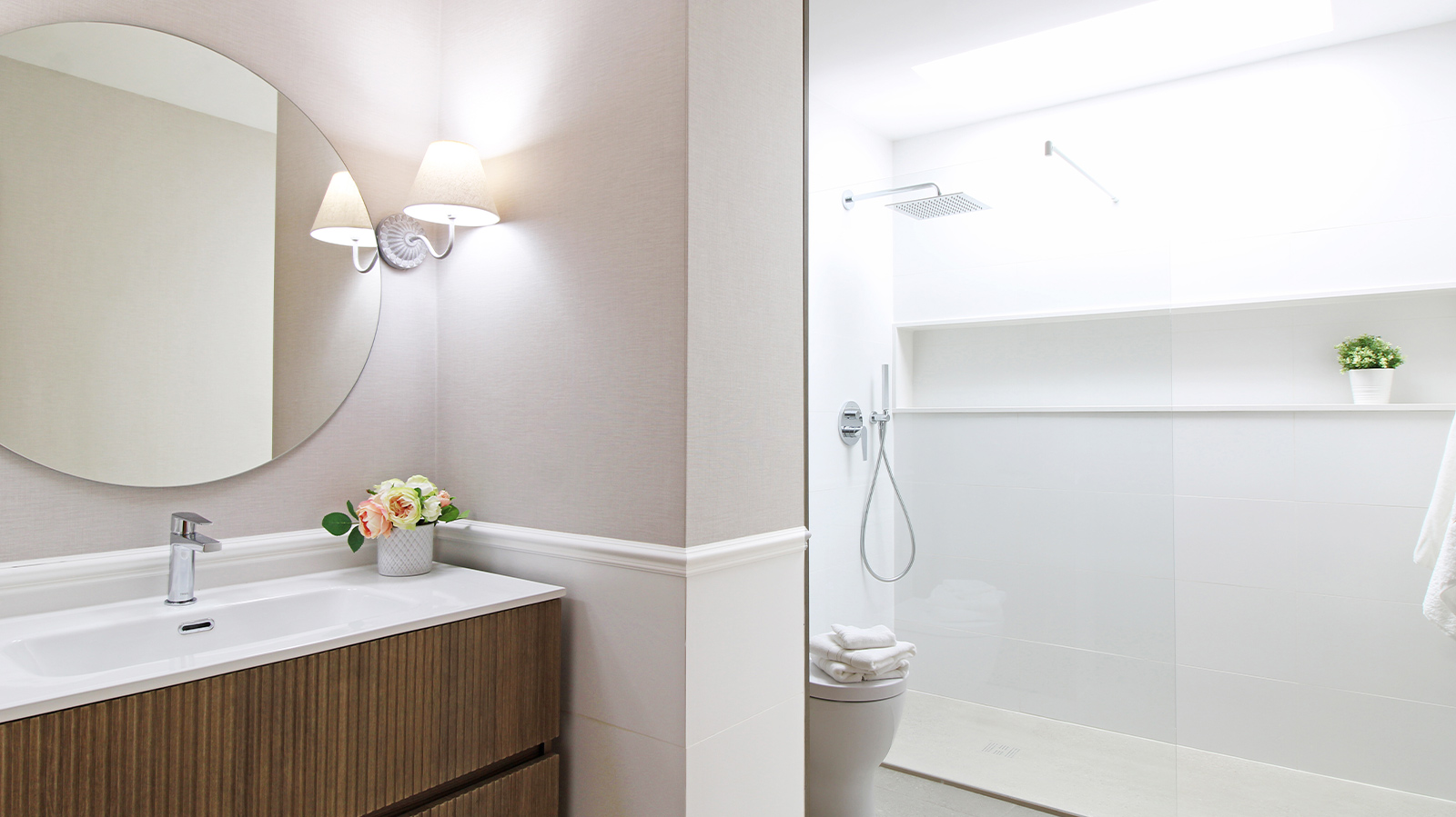 Baño luminoso con espejo redondo sobre lavamanos y ducha amplia